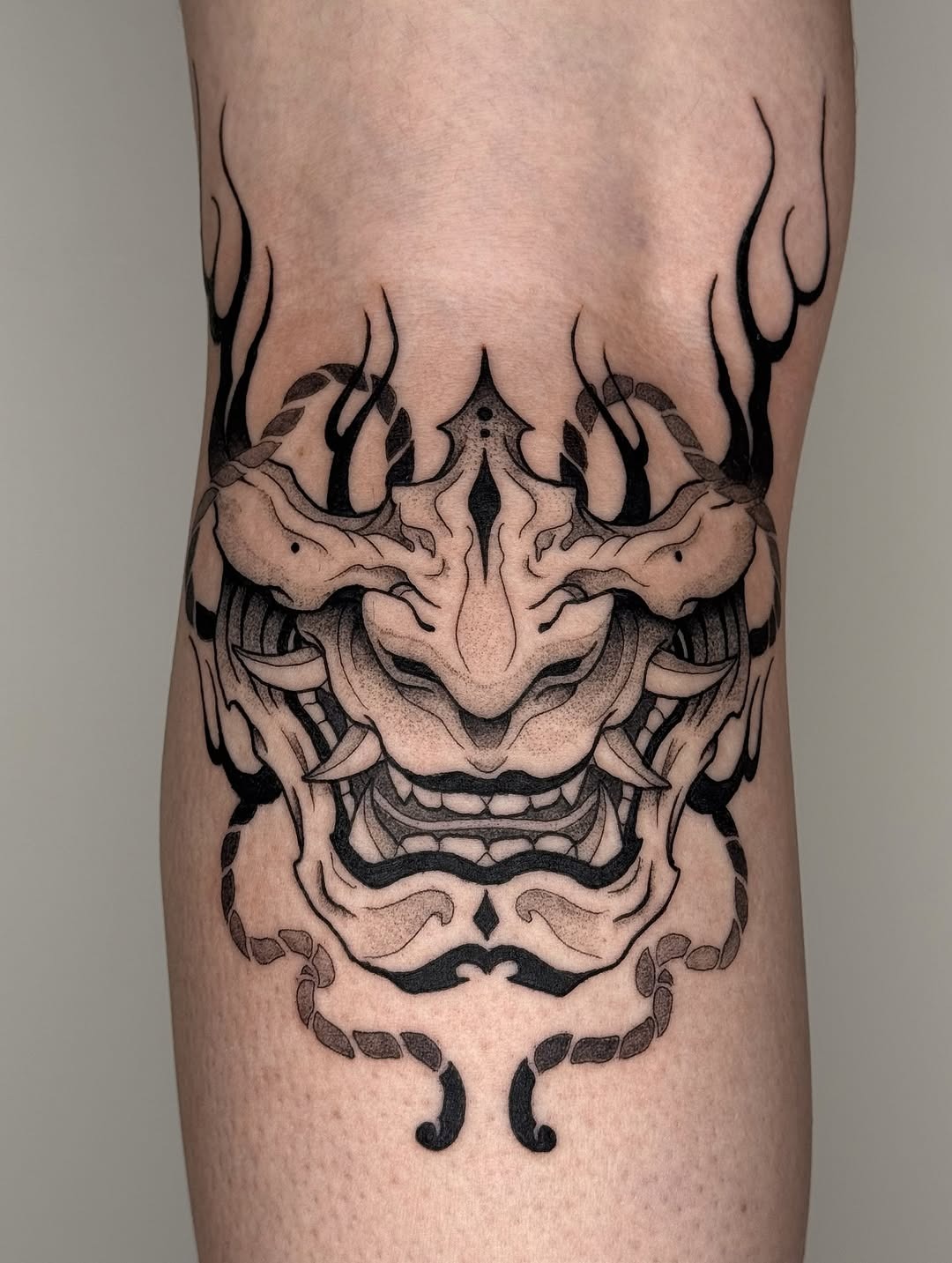 This stunning dotwork tattoo features a fierce mythical mask, showing intricate patterns and bold contrasts.