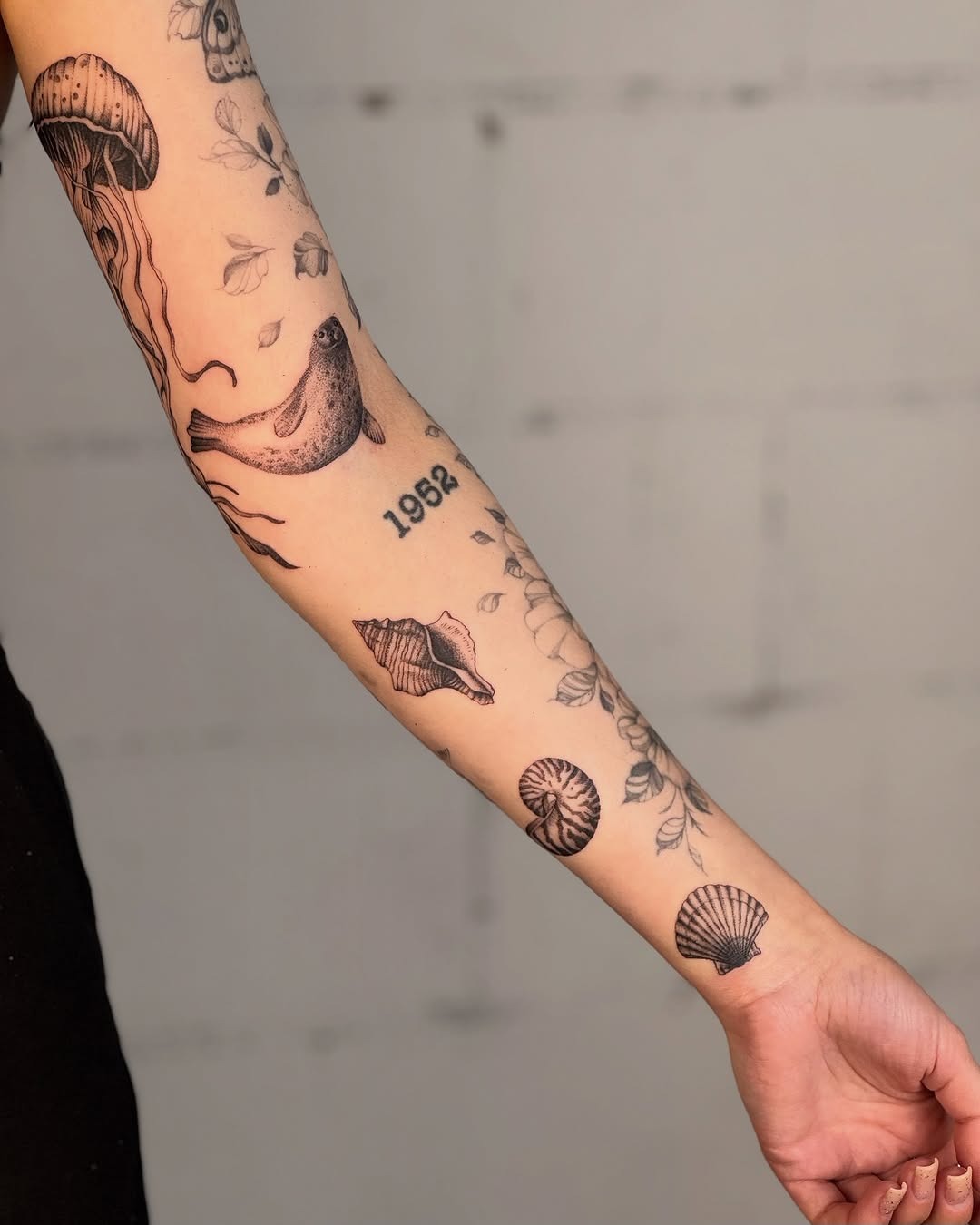 This arm tattoo features beautiful dotwork designs of jellyfish, seashells, and delicate flowers, creating an underwater vibe.