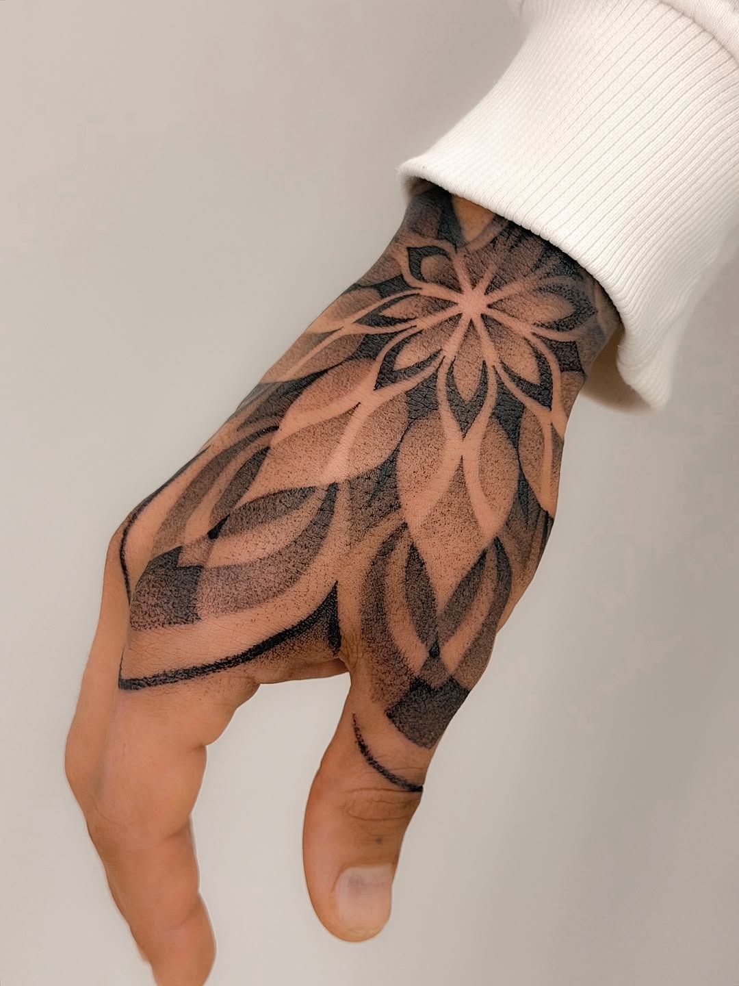 This stunning dotwork tattoo wraps gracefully around the hand, creating an intricate floral design.