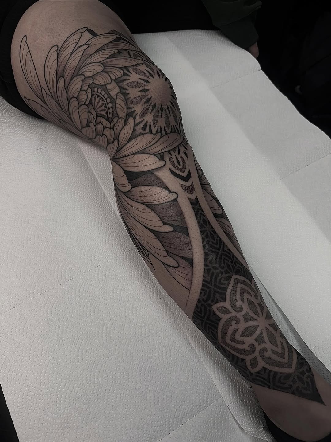 This stunning leg tattoo features intricate dotwork patterns intertwined with beautiful floral designs.