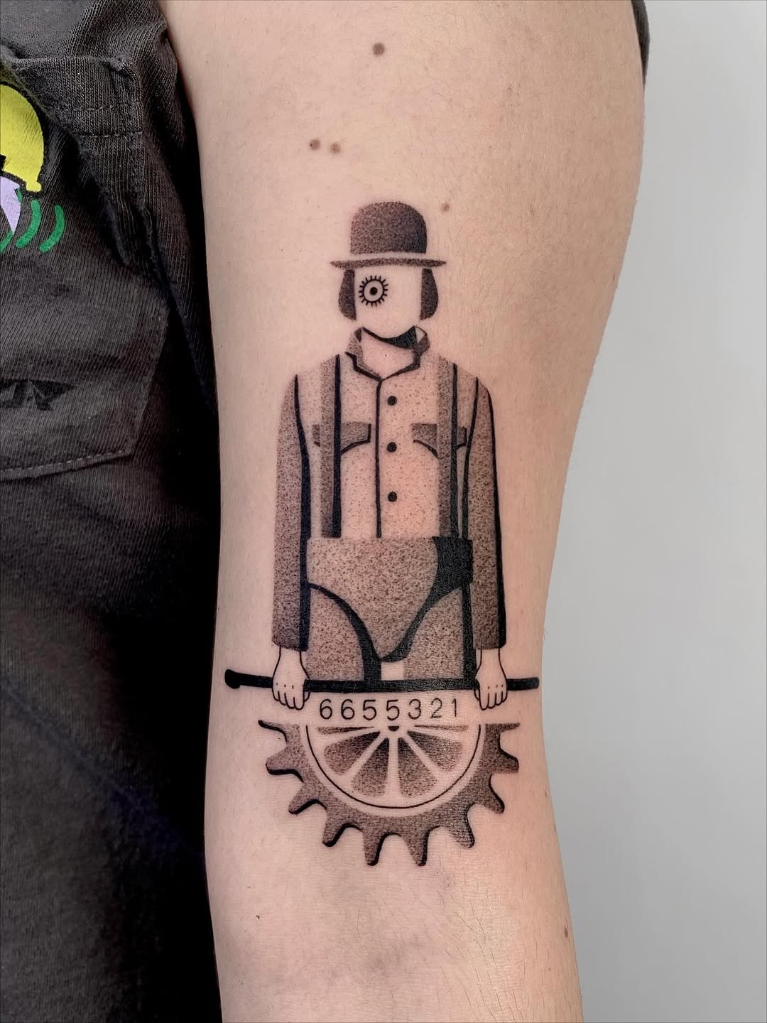 This dotwork tattoo showcases a unique mechanical character holding a gear and sporting a vintage hat.