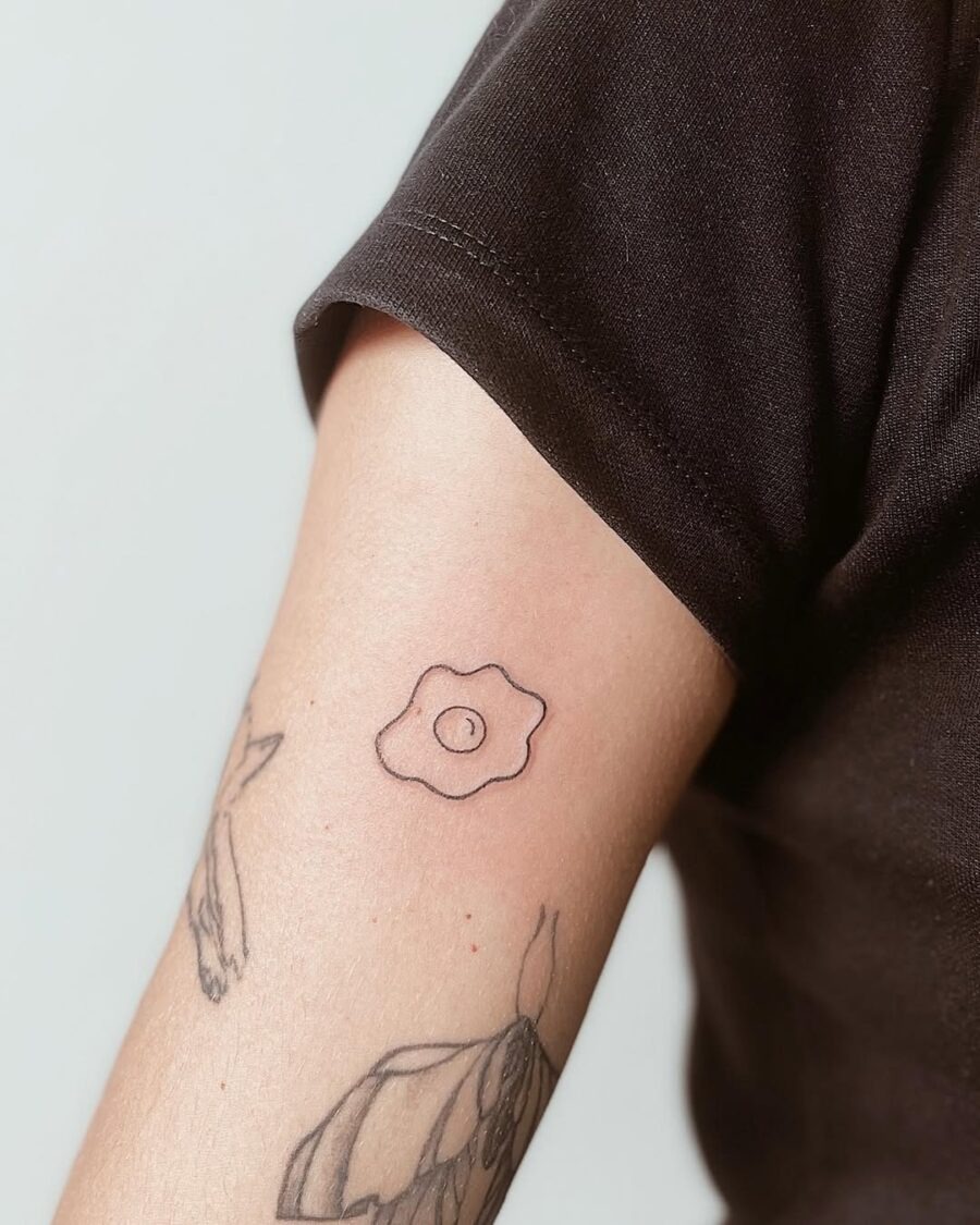 This tattoo features a simple, outlined design of a fried egg, set against a soft background.