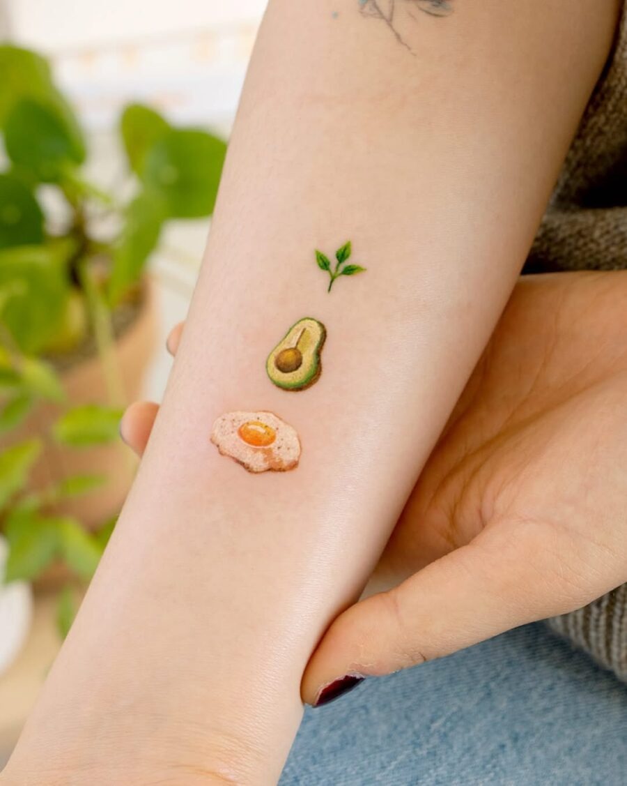 This unique tattoo features a stylized avocado and an egg, showing colors and fine details.