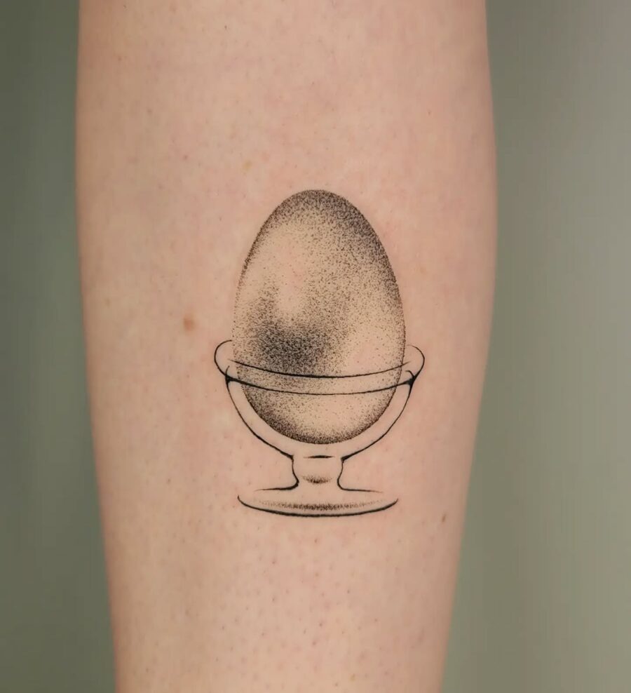 This tattoo showcases a beautifully simplistic egg nestled in a bowl, exuding a calm yet intriguing vibe.