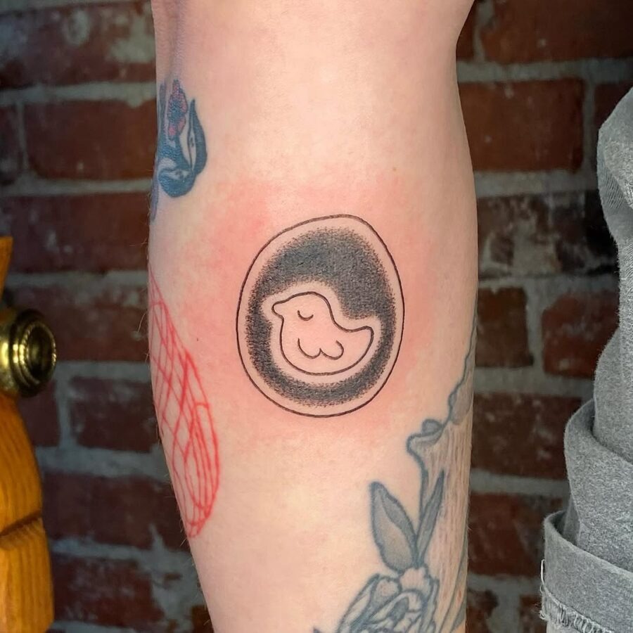 This tattoo features a charming little bird nestled in an egg shape.