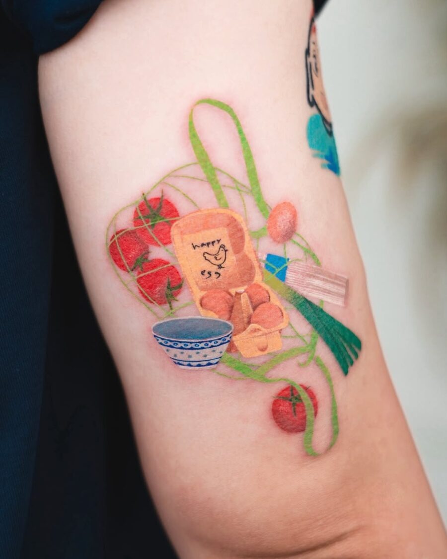 This tattoo features a cheerful, cartoon-like egg character surrounded by fresh tomatoes and playful greens, giving it a fun, lively vibe.