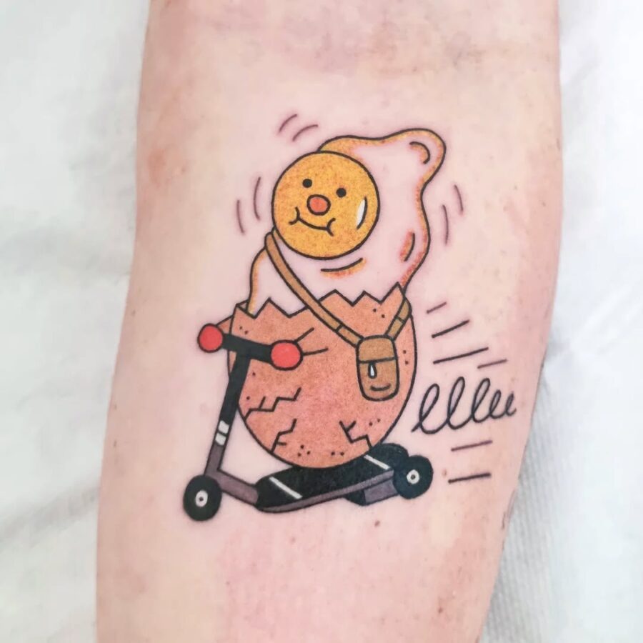 This whimsical tattoo features a cheerful egg character riding a scooter, capturing a sense of joy and adventure.