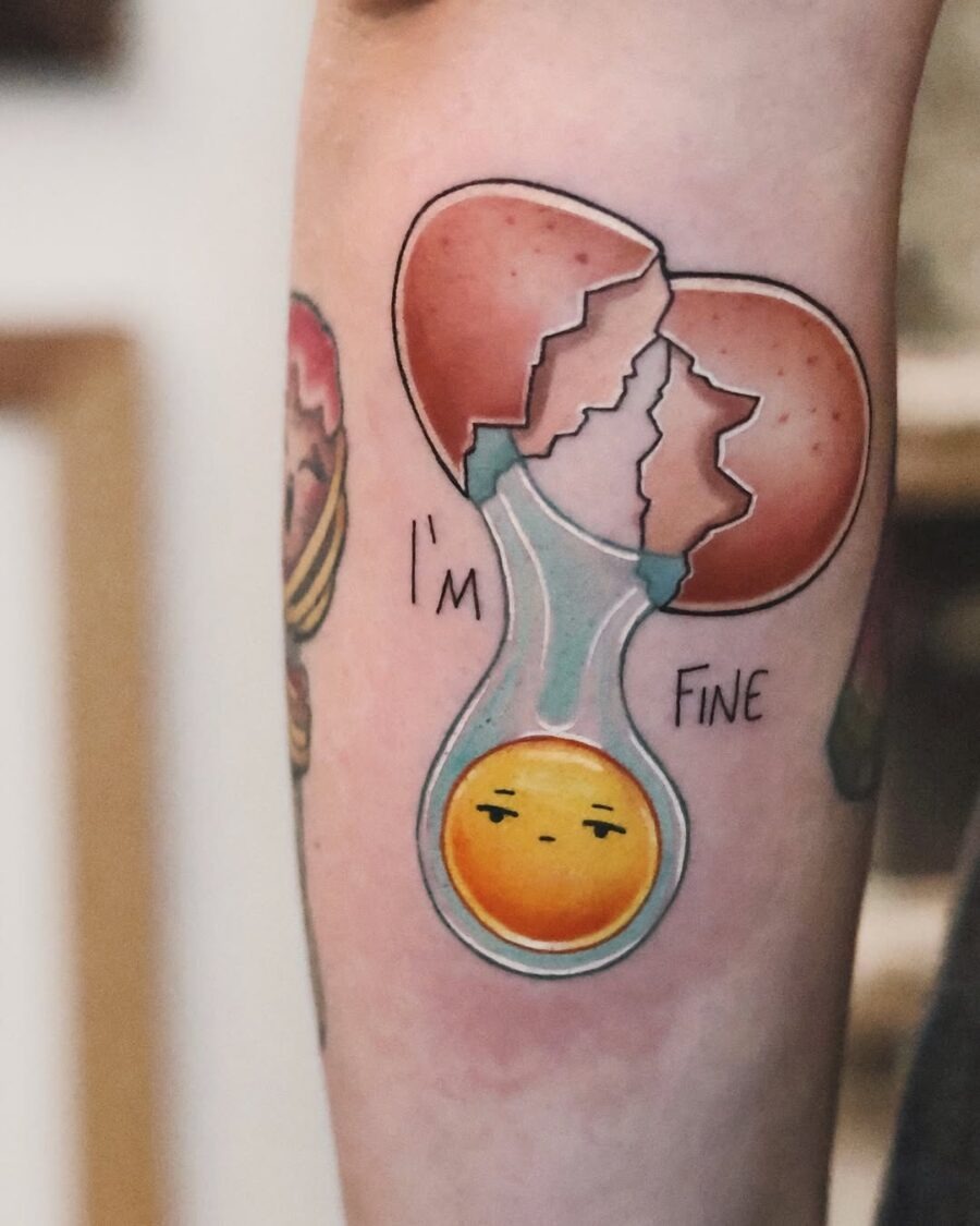 This egg tattoo showcases a cracked shell revealing a cute, expressive yolk inside.