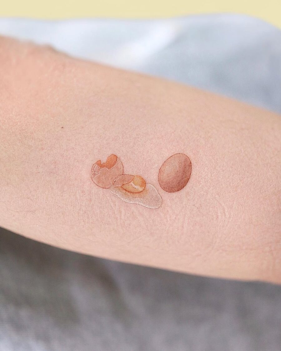 This tattoo features a beautifully realistic depiction of an egg and a broken eggshell on an arm.