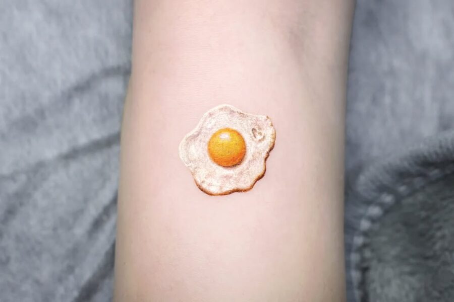 This tattoo showcases a beautifully detailed fried egg, complete with a perfectly golden yolk.