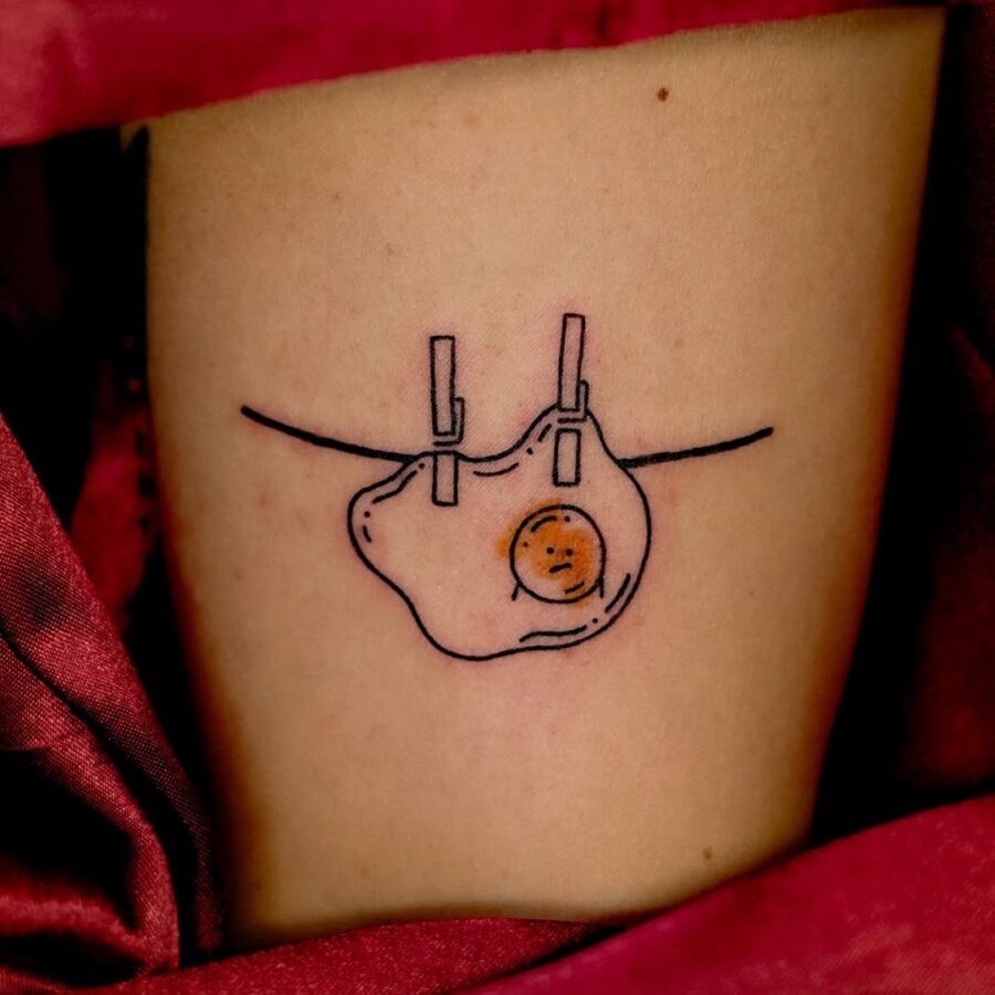 This tattoo features a whimsical illustration of a fried egg hanging on a clothesline.
