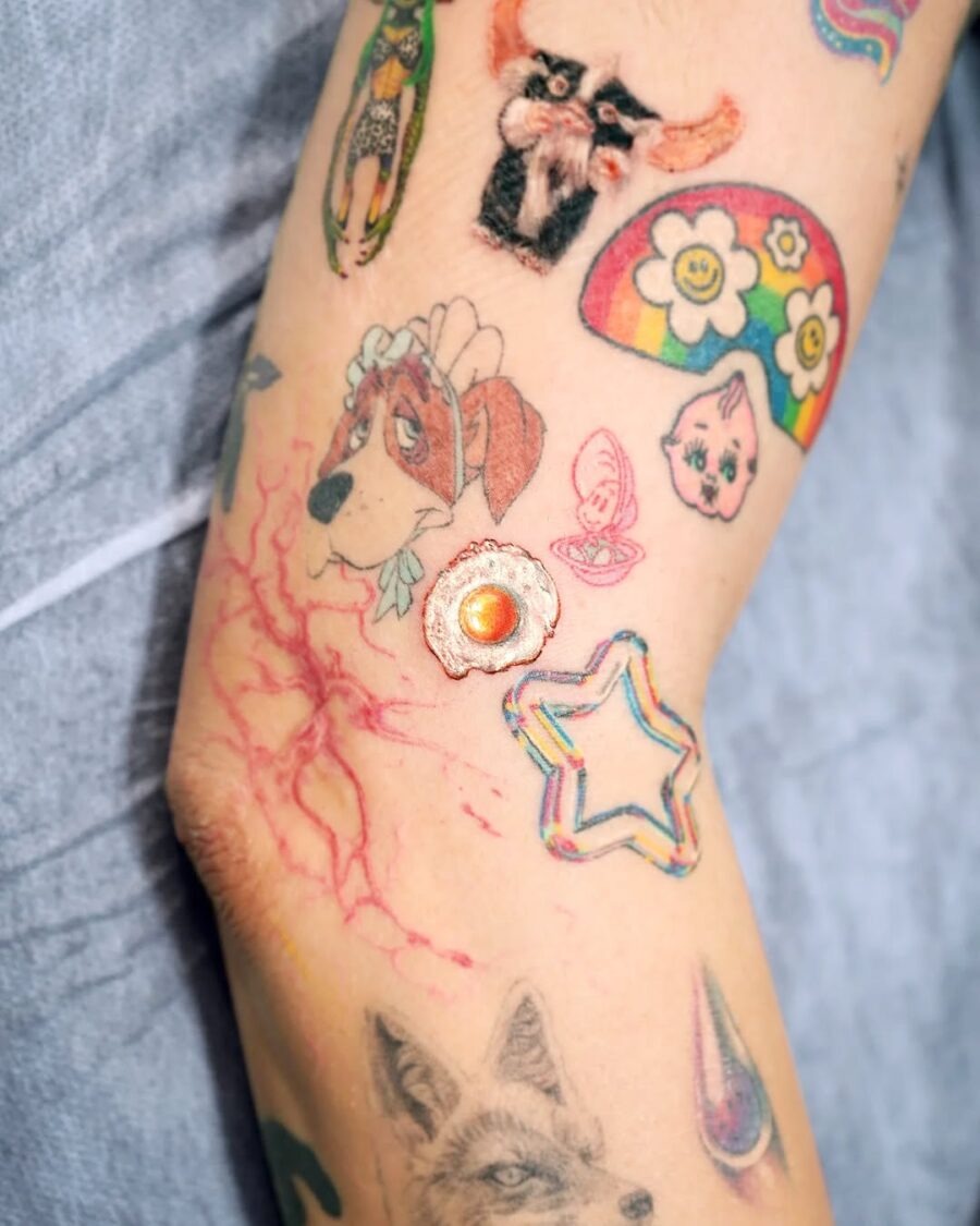 This colorful tattoo features a creative egg design, surrounded by playful motifs like a dog, flowers, and a star.