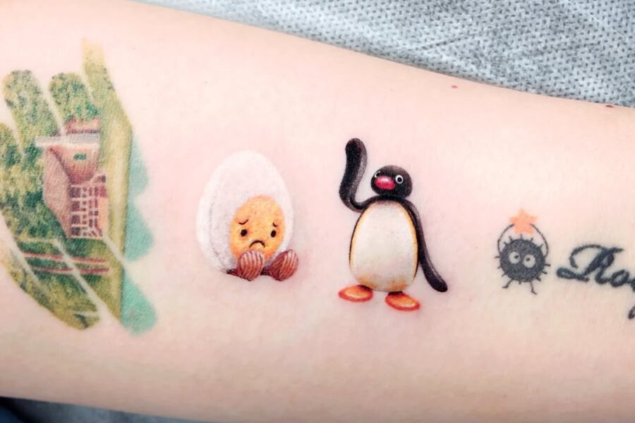 This tattoo features a whimsical sad egg alongside a cheerful penguin, capturing a playful yet emotional narrative.