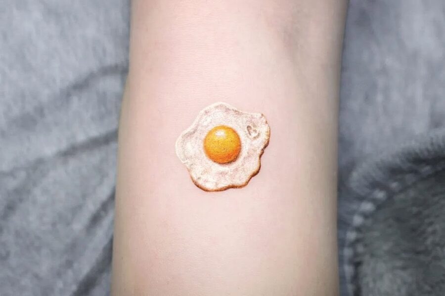 This tattoo features a realistic depiction of a fried egg, complete with a yellow yolk.