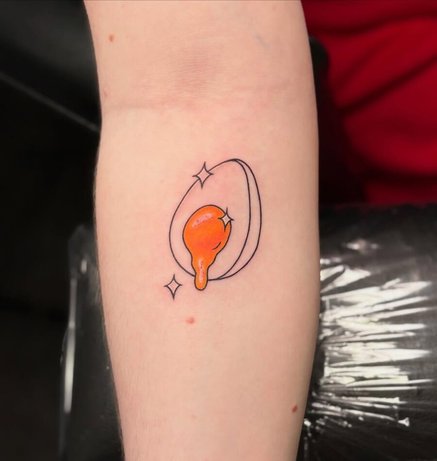 This egg tattoo features a bold design with an orange yolk that pops against the subtle outer egg shell.