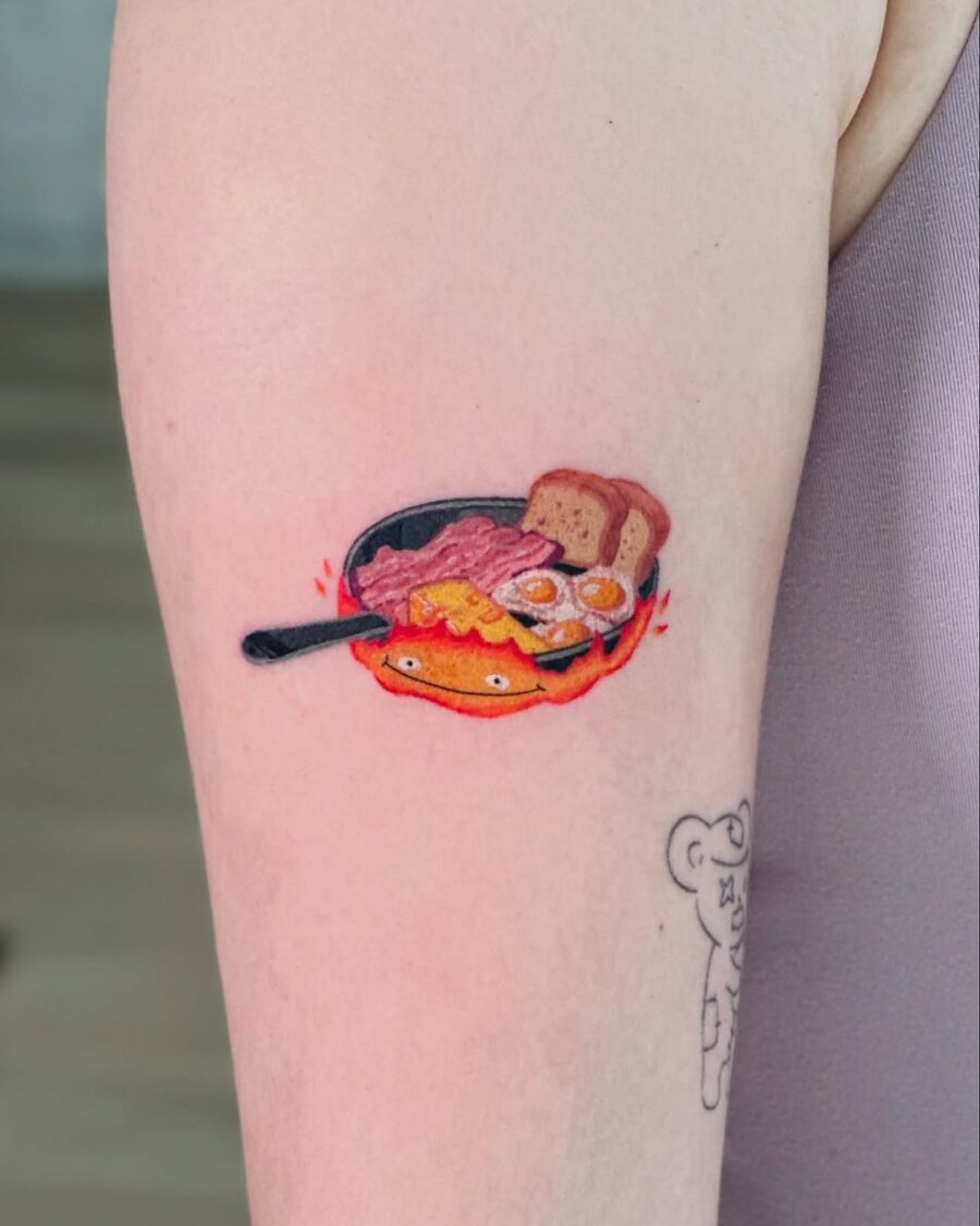 This playful tattoo showcases a sunny-side-up egg nestled on a plate, accompanied by bacon and toast.