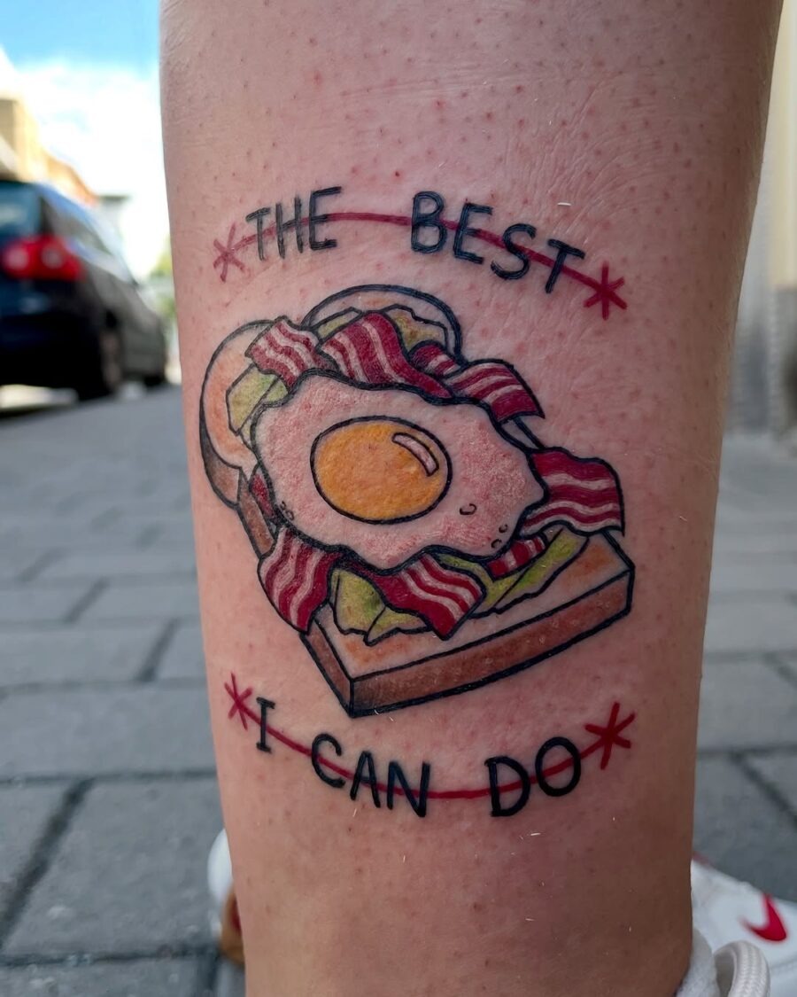 This quirky tattoo features an egg on a bacon sandwich with the phrase 'The Best I Can Do.' It combines food and fun in a playful design.
