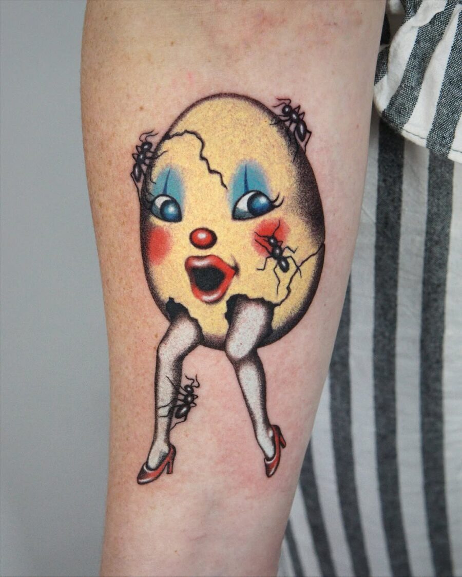 This tattoo showcases a, playful design of a cracked egg character with a cheerful expression.