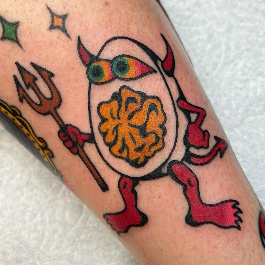 This eye-catching egg tattoo showcases a playful monster with devilish horns and a mischievous grin.