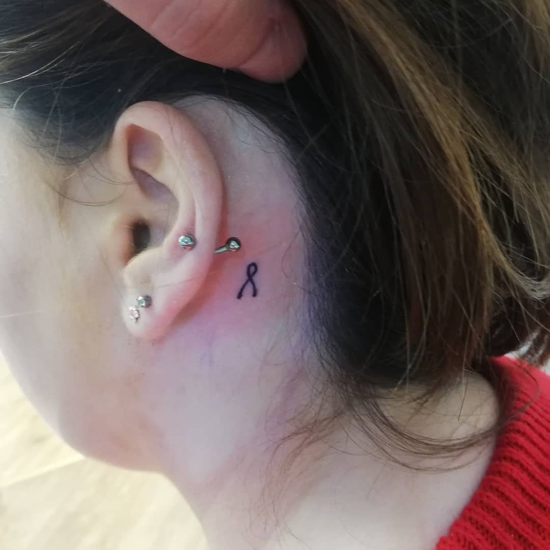 A subtle black ribbon tattoo behind the ear Tattoo Design
