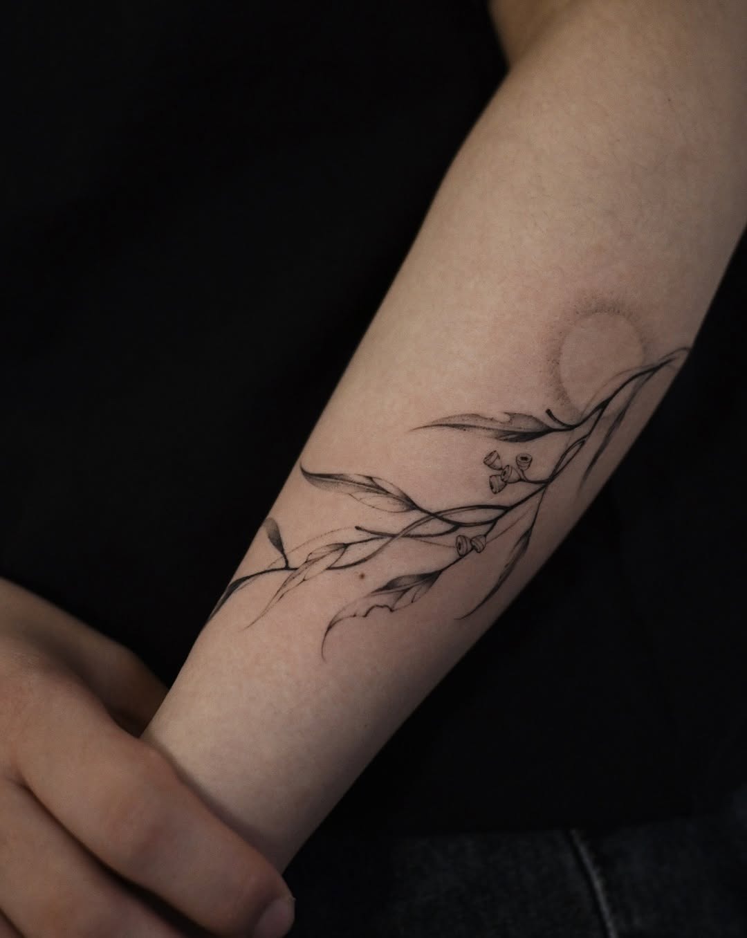 Elegant eucalyptus branch tattoo with a subtle sun Tattoo Design