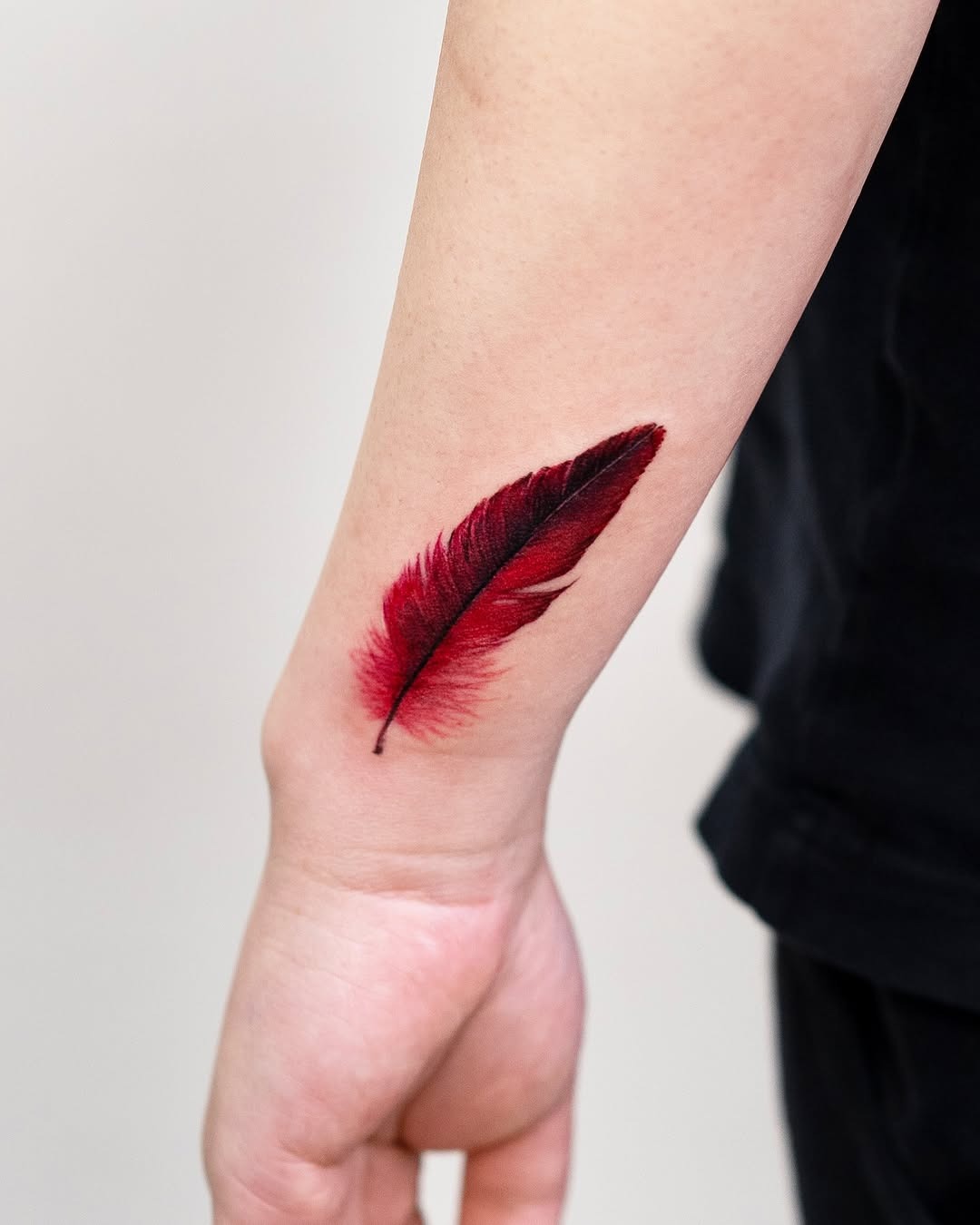 Bold red feather tattoo on forearm Tattoo Design