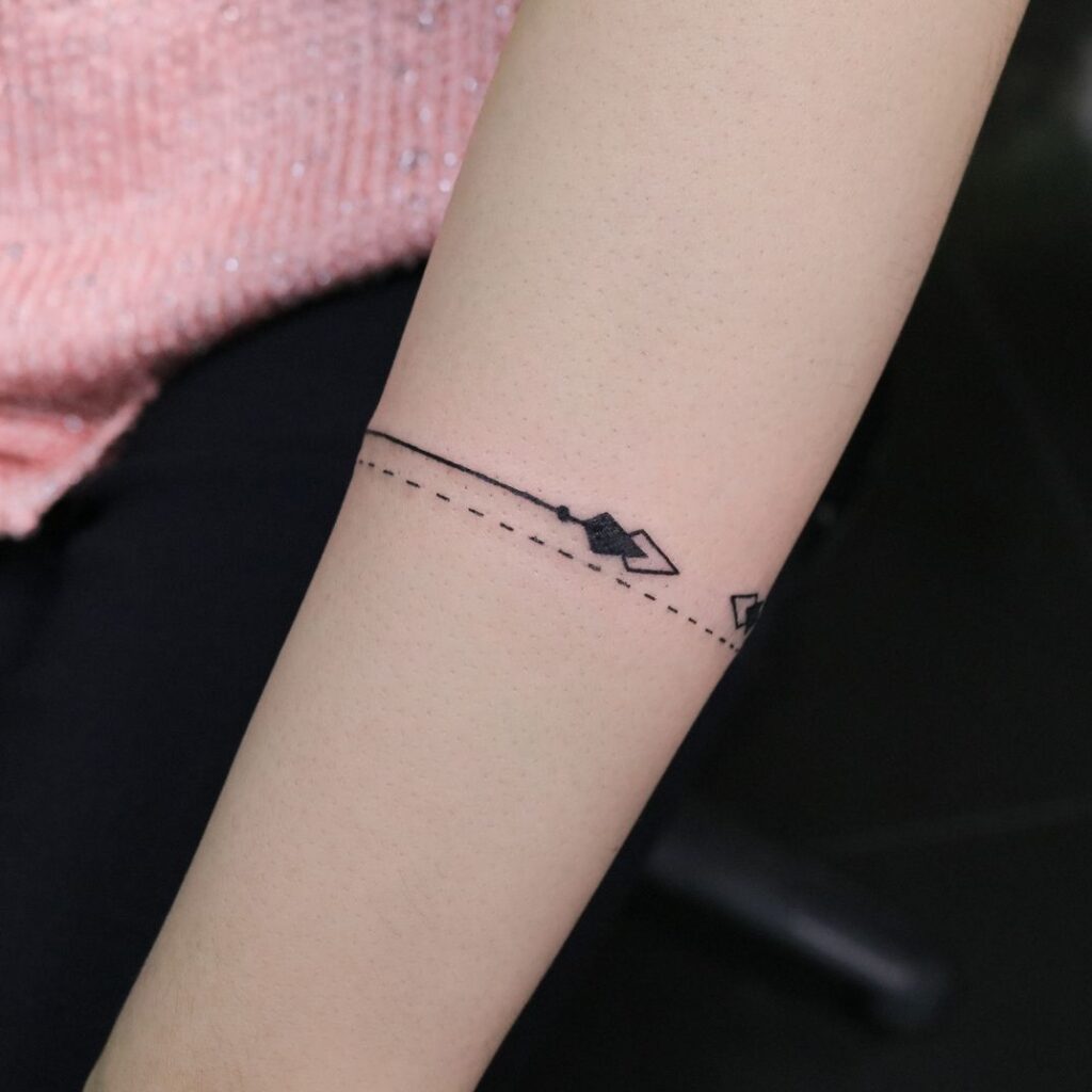 Thin arrow and dot band tattoo wrapping around the wrist like a bracelet