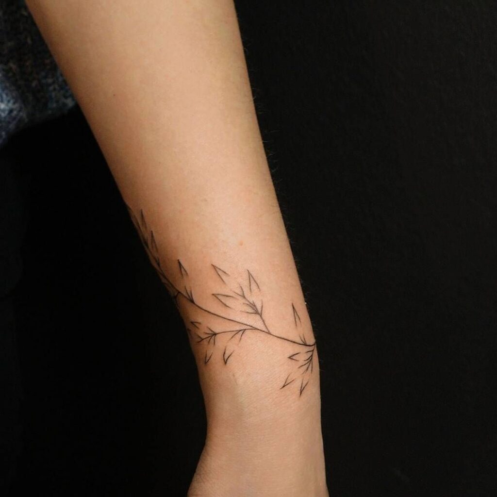Slender fine line branch with leaves tattoo along the forearm