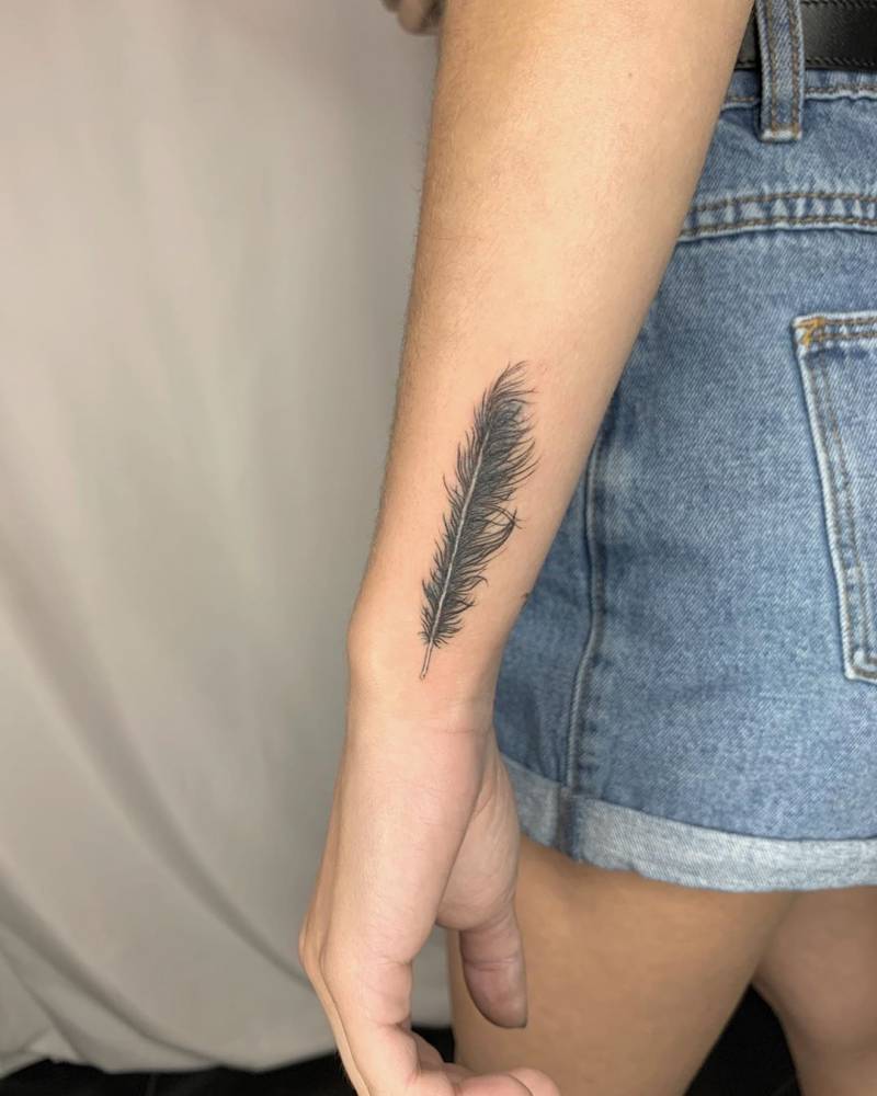 Single fine line feather tattoo on the forearm near the wrist