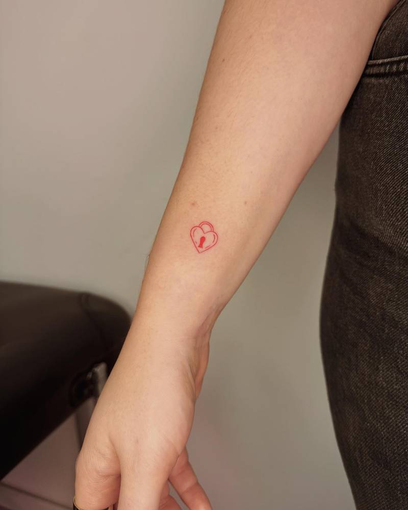 Fine line heart padlock tattoo just above the wrist on the inner forearm
