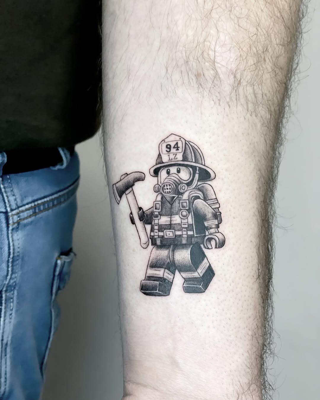 This tattoo features a unique LEGO-style firefighter with a detailed helmet and axe.