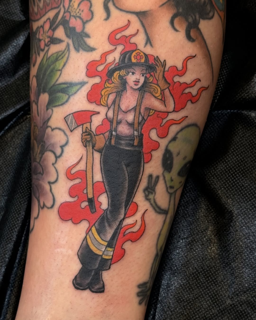 This tattoo features a pinup girl firefighter, complete with an axe and bold colors.