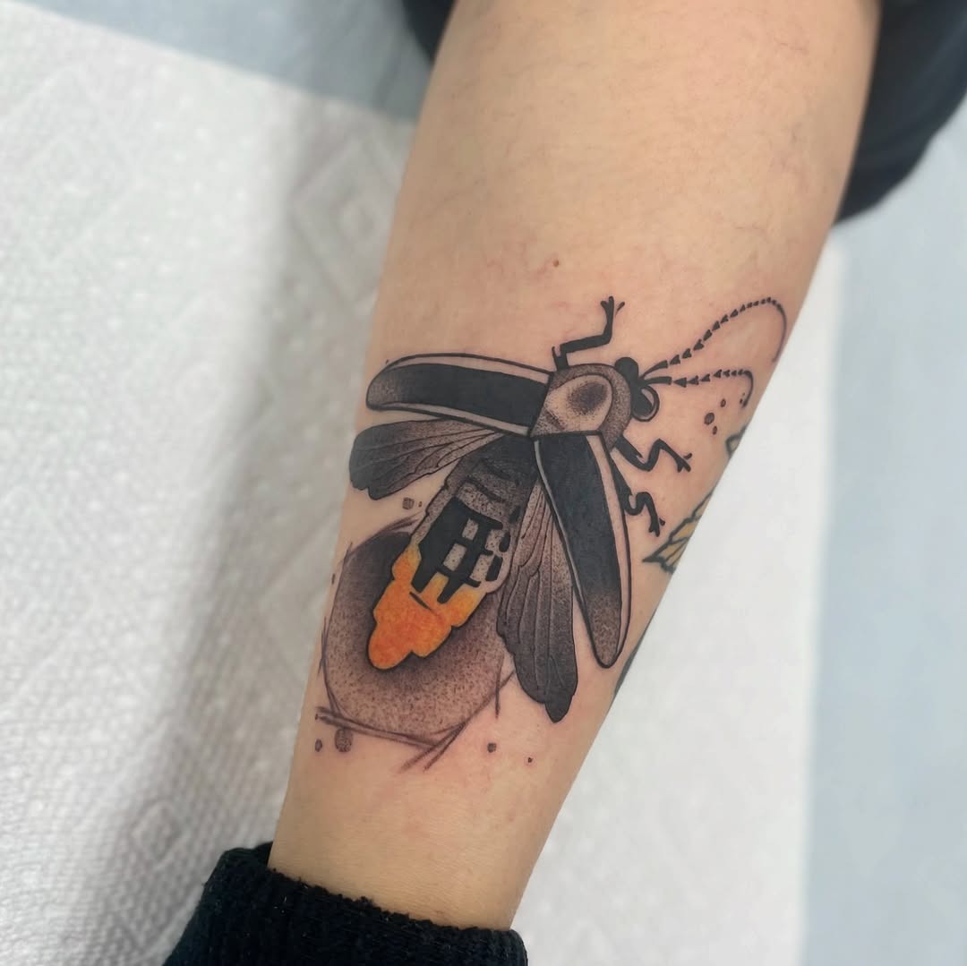 This unique firefly tattoo features an intricate design with shimmering black and orange hues.