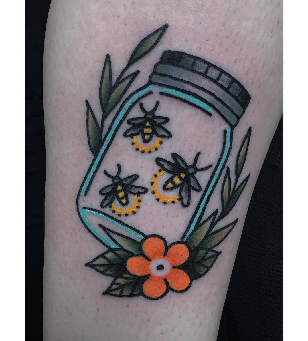 This lively tattoo features fireflies captured within a glass jar, surrounded by lush green leaves and a bright orange flower.