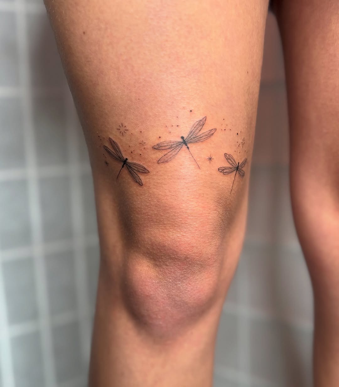 This tattoo showcases delicate fireflies dancing around the knee.