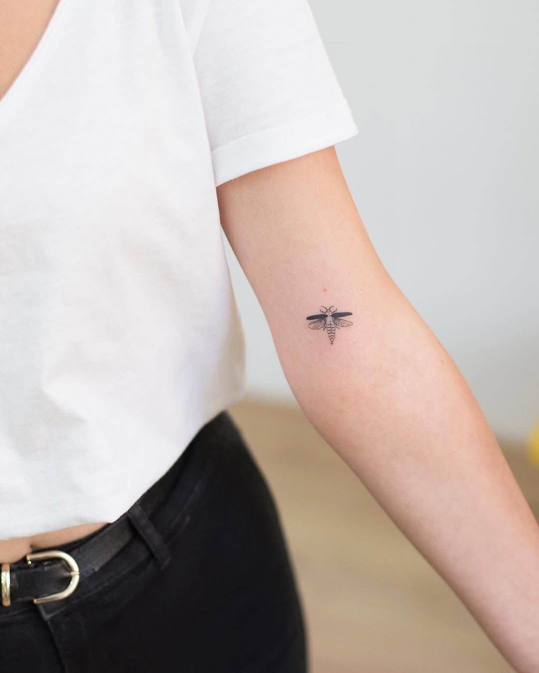 This small firefly tattoo features delicate detailing, showing its wings and body with subtle shading.
