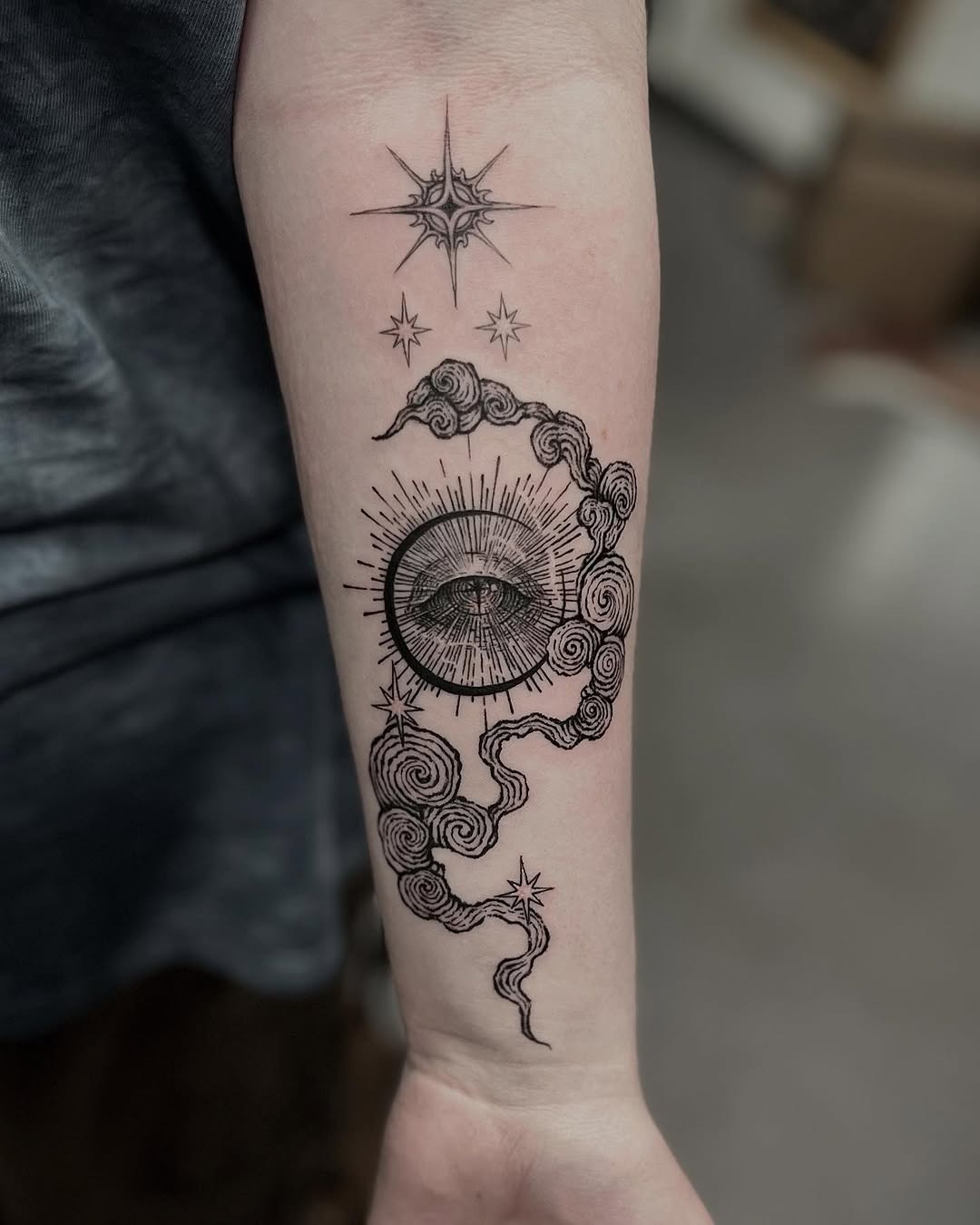 This forearm tattoo features a beautifully crafted sun and moon entwined within swirling clouds.