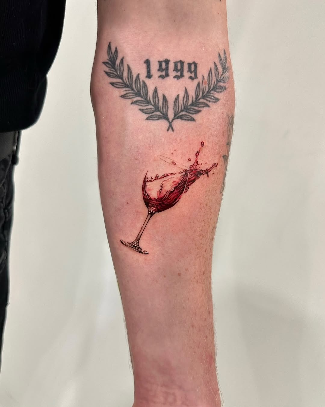 This forearm tattoo features a red wine glass, elegantly capturing the splash of liquid.