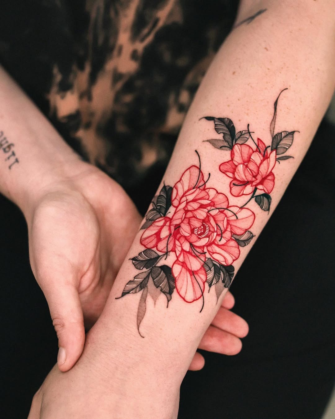 This forearm tattoo features striking red flowers intertwined with elegant black outlines.