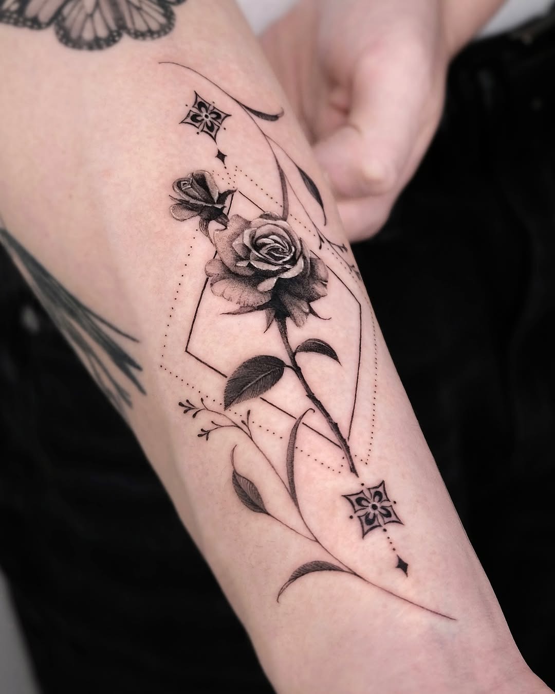 This forearm tattoo showcases a beautifully detailed black rose, entwined with graceful flowing lines.