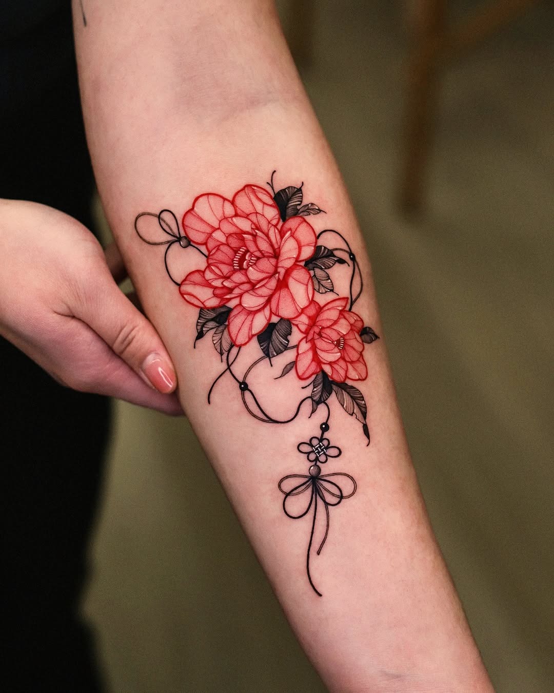 This stunning forearm tattoo features red flowers intertwined with delicate black lines.