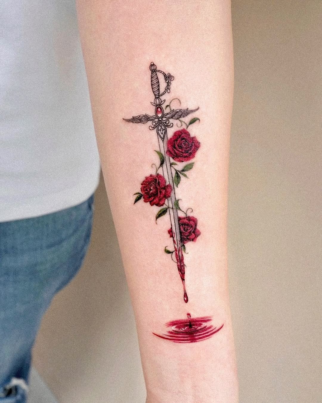 This forearm tattoo features a beautifully designed sword surrounded by lush roses, dripping with a hint of red.