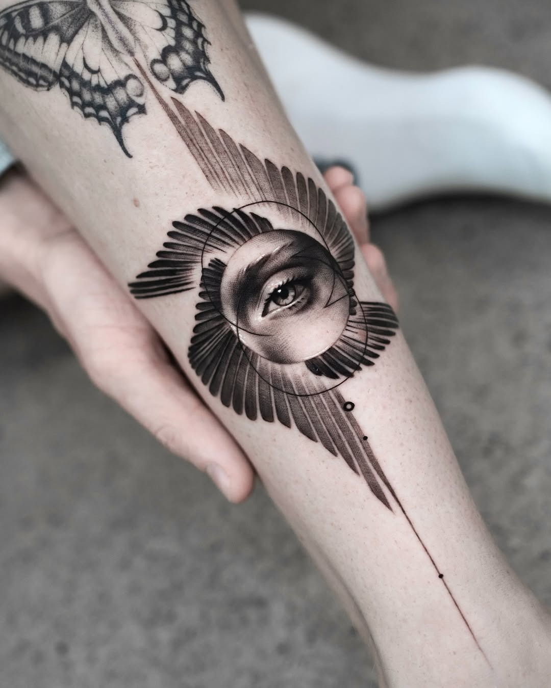 This tattoo showcases a mesmerizing eye surrounded by detailed feather-like patterns.