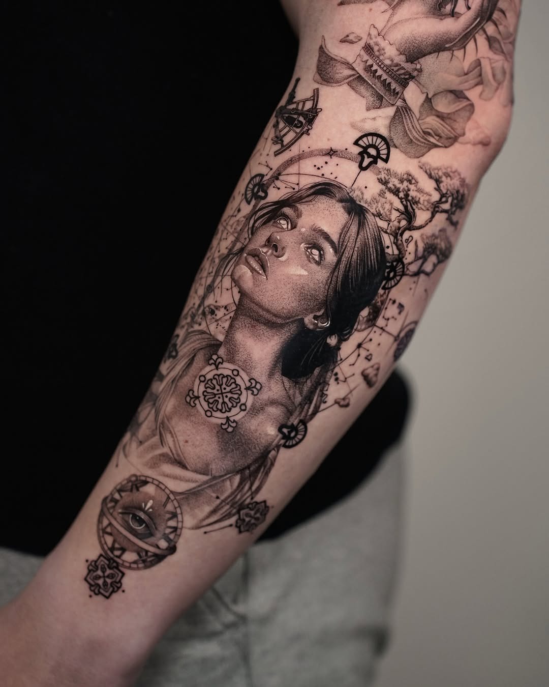 This forearm tattoo features a detailed portrait of a woman, surrounded by intricate elements like floral designs and geometric shapes.