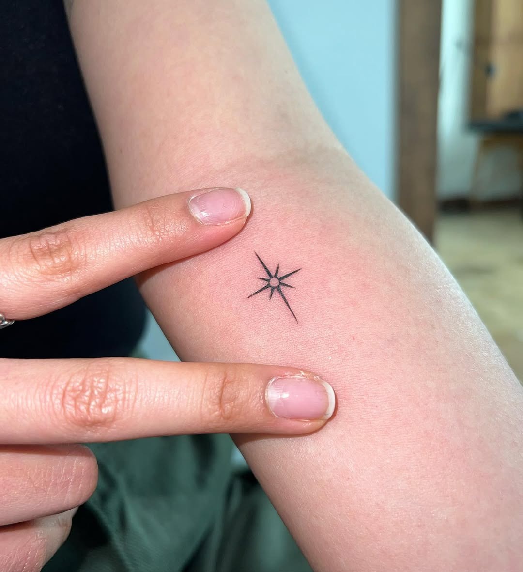 This tattoo features a minimalist star design on the forearm.