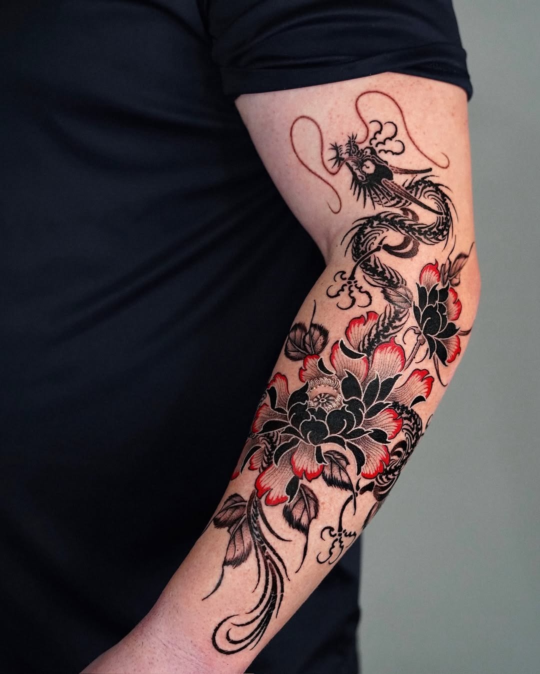 This forearm tattoo features an intricate design combining a fierce dragon with elegant flowers.