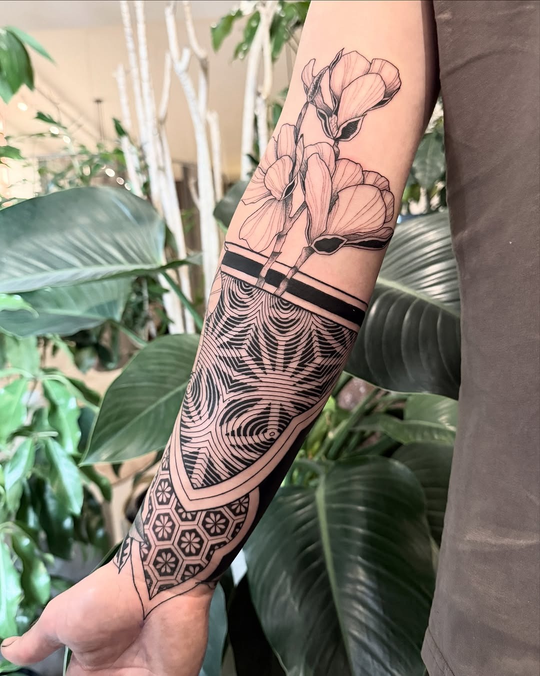 This forearm tattoo combines beautiful floral elements with intricate geometric shapes.