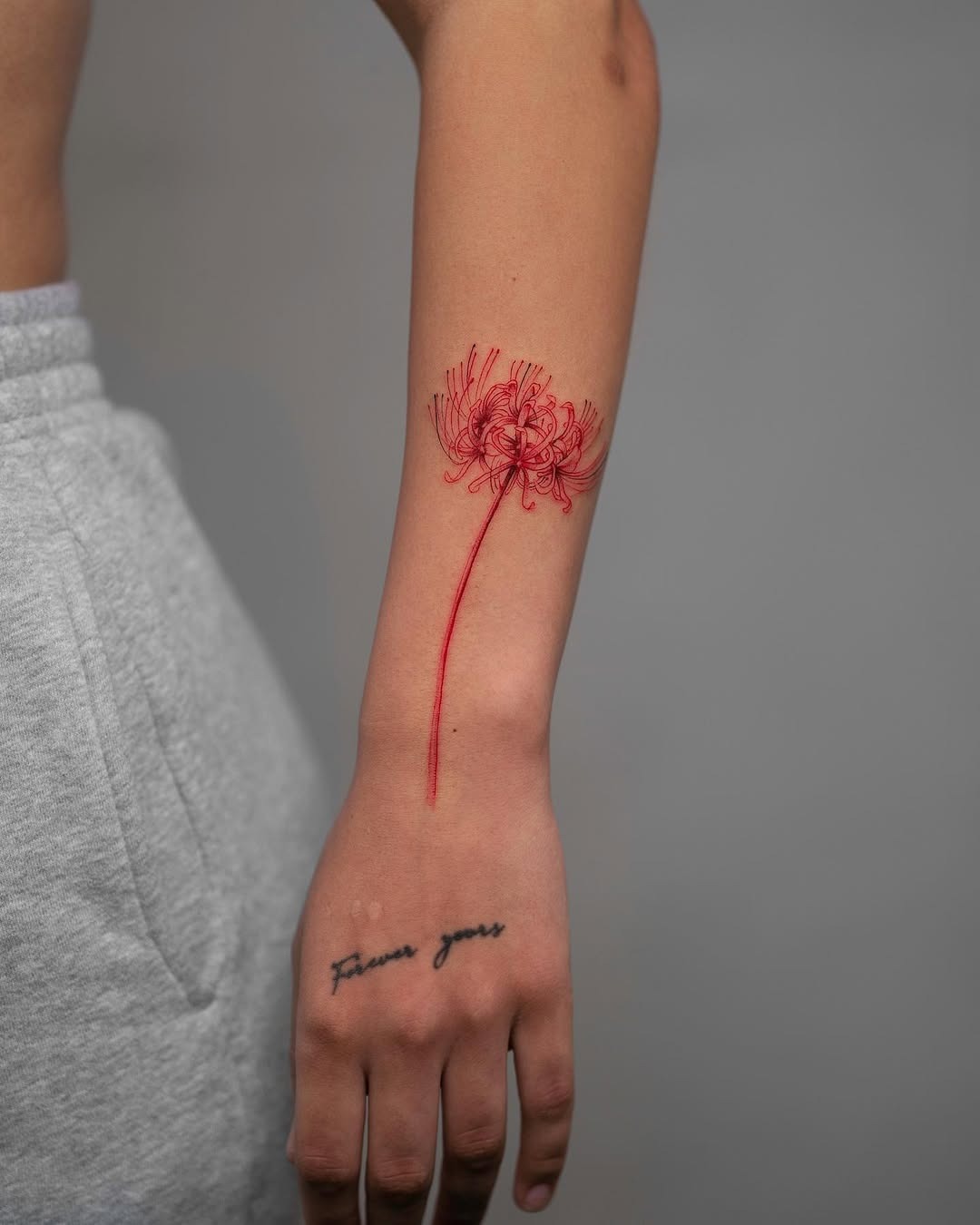 This delicate red flower tattoo elegantly wraps around the forearm, showing a minimalist design.