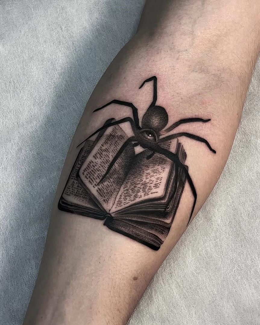 This forearm tattoo features a striking design of an open book with a spider perched on top.