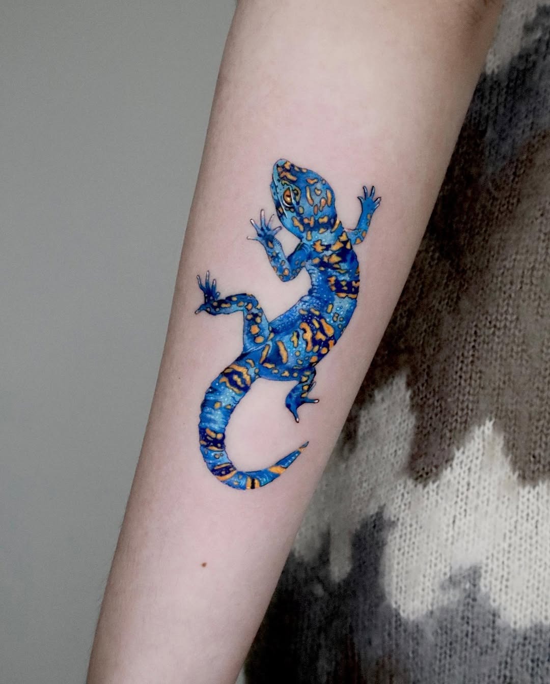 This stunning forearm tattoo features a colorful gecko, detailed with intricate patterns and hues.